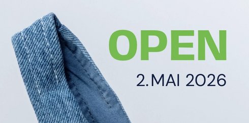 Ein Banner mit dem großen Text "OPEN" und dem Datum "2. MAI 2026". Darunter steht: "Wir freuen uns, Sie auch am Samstag von 10-14 Uhr zu begrüßen!" Im Hintergrund ist ein Teil eines blauen Stoffes sichtbar.